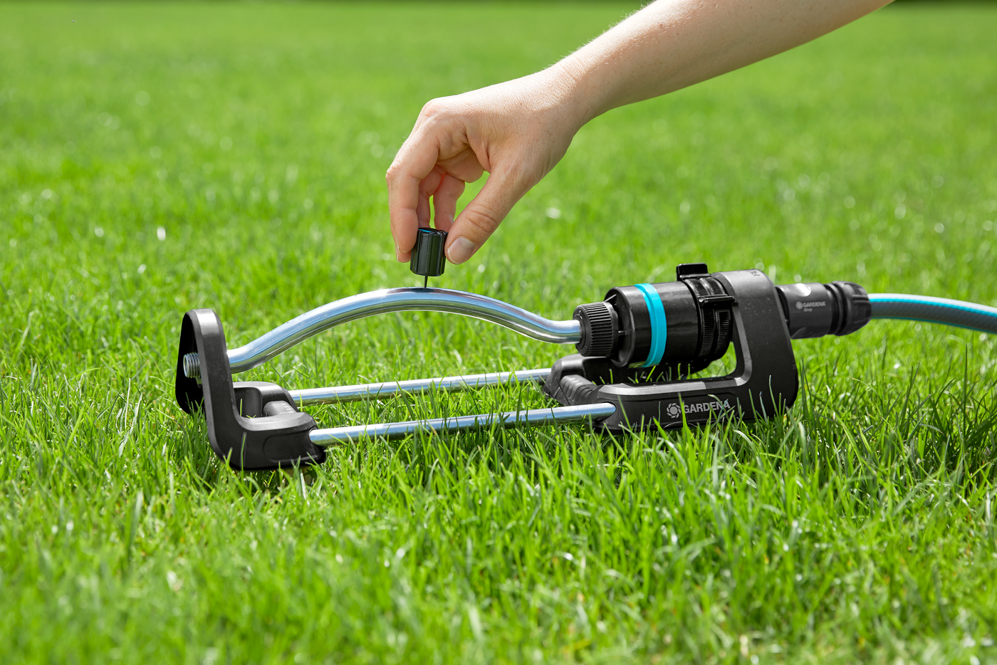 A person adjusting a Gardena lawn sprinkler on a grassy lawn.