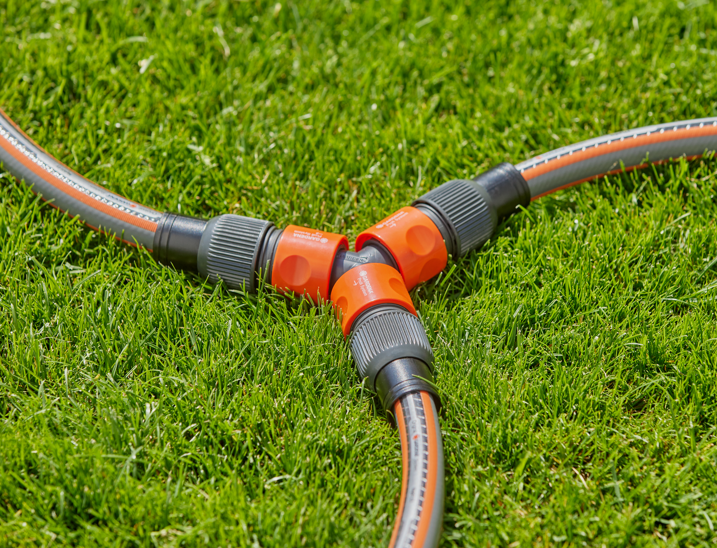 Three garden hoses connected with Gardena hose connectors on a grassy lawn.
