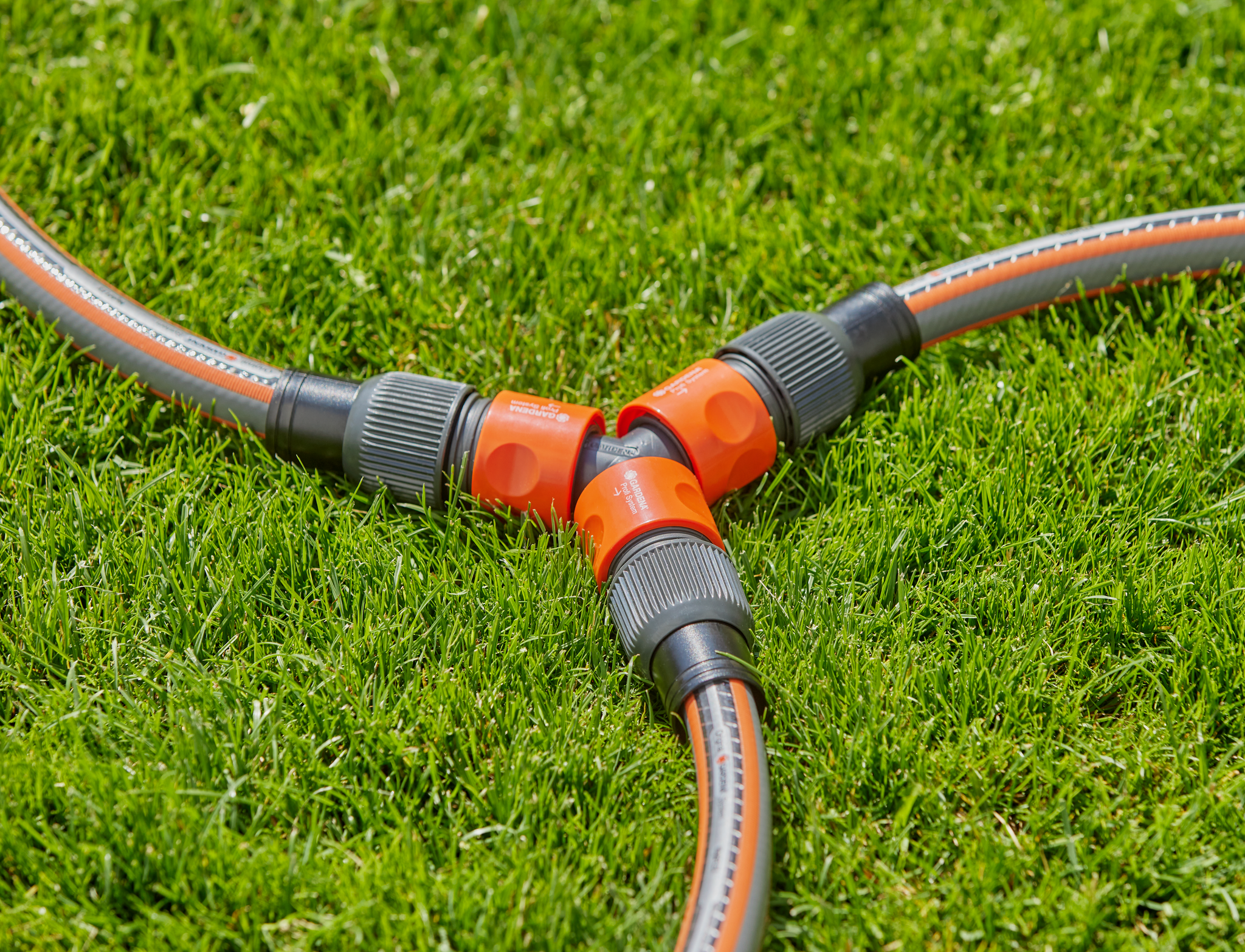 Three garden hoses connected with Gardena hose connectors on a grassy lawn.
