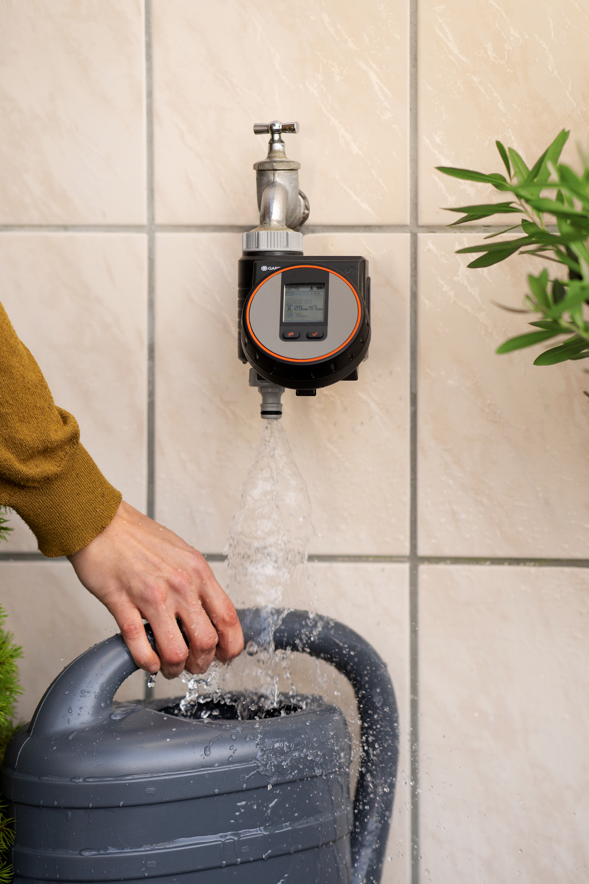 A person filling a watering can using a tap with a digital water timer attached.