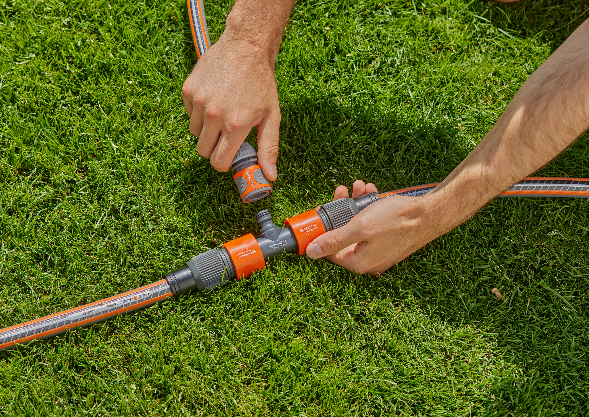 Hands connecting Gardena hose fittings on a grassy lawn.