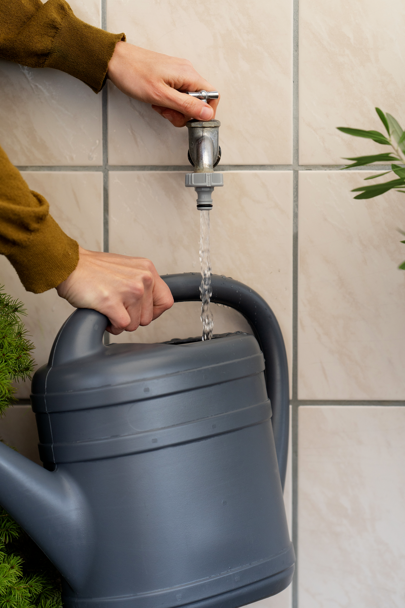A person filling a watering can from a wall-mounted faucet.