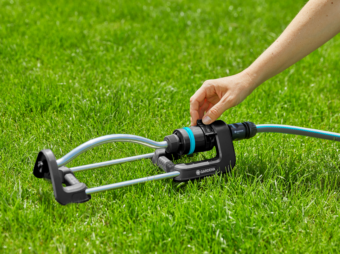 A person adjusting a Gardena garden sprinkler on a grassy lawn.