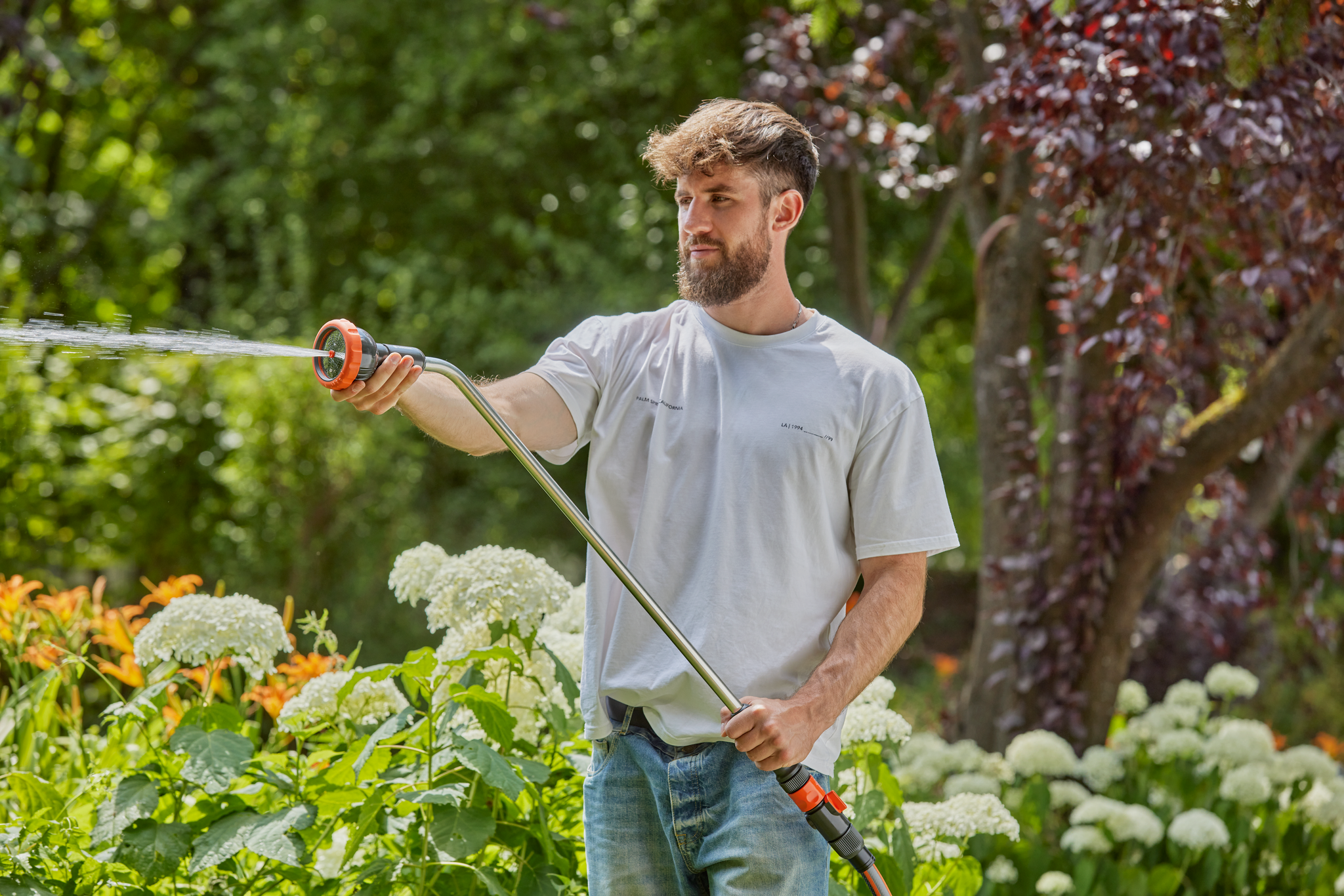 A person watering plants in a garden using a Gardena hose nozzle.