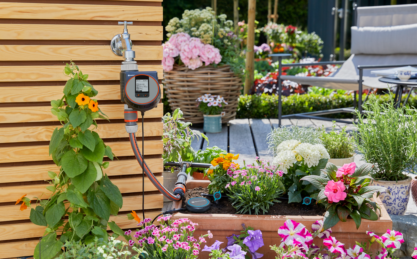 Gardena smart irrigation system in a garden setting with various flowers and plants.